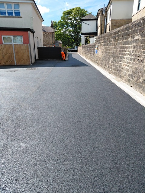 Newly surfaced back lane with fresh white lining beside a stone wall