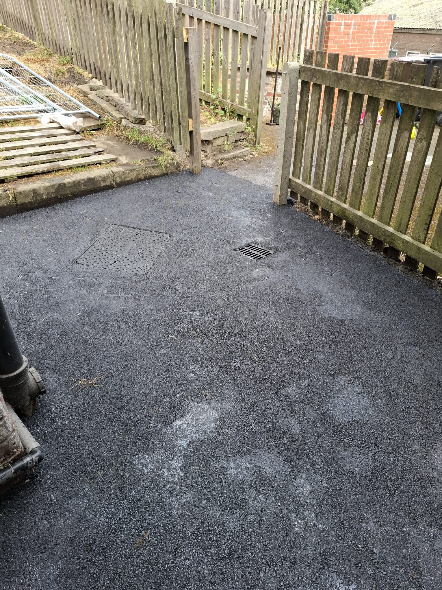 Tarmac laid to falls around a manhole cover and gully in a rear yard, Sheffield